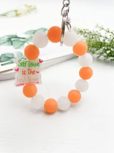Detalle de llavero tipo pulsera de cuentas de silicona con dije 'Self Love'.