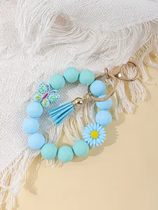 Detail view of a light blue silicone bead wristlet keychain with daisy and tassel charms