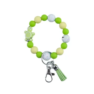 Cute green silicone bead wristlet keychain with turtle charm and tassel on white background.