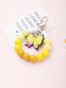 Close-up of yellow silicone beaded wristlet keychain with a teacher-themed pencil bow charm.