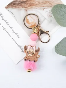 Detailed view of cartoon cow keychain with pink silicone beads and fluffy pom-pom