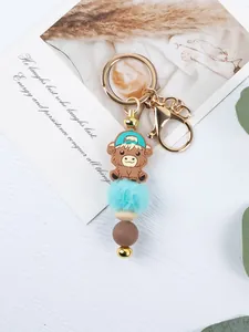 Detailed view of cartoon highland cow keychain with turquoise pom pom and silicone beads