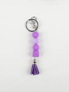 Detailed view of purple silicone beads and tassel keychain on white textured surface