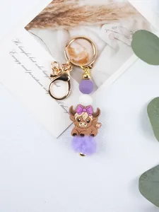 Detail of a purple highland cow keychain with silicone beads and a soft pom-pom.
