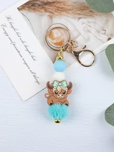 Detail shot of a cartoon highland cow keychain with turquoise pom-pom and blue beads.