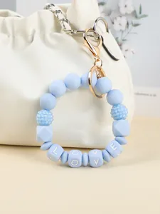 Detailaufnahme eines blauen Silikon-Schlüsselanhängers mit LOVE-Perlen an einer Tasche.