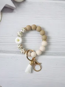 Detailed view of a daisy silicone bead bracelet keychain with white tassel on wood background.