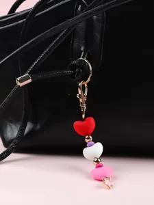 Détail d'un charme en perles de silicone en forme de cœur sur un sac en cuir noir.