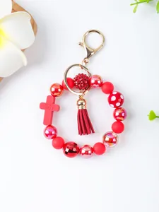 Macro detail of red silicone bead keychain with cross charm and tassel decoration