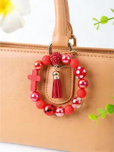 Detailed view of red silicone beaded keychain with cross and tassel charm on a tan bag
