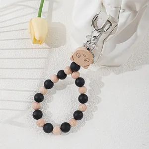 Silicone and wood beaded keychain wristlet with laser-engraved charm attached to bag