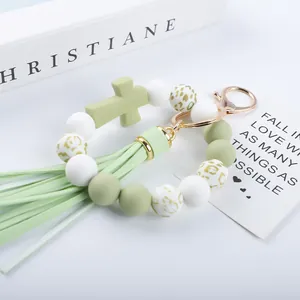 Detail view of sage green silicone beaded keychain with cross charm and stylish tassel.