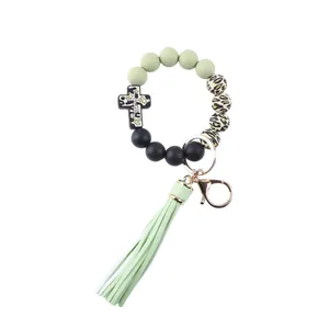 Detailed macro view of the silicone beaded keychain featuring a cross charm and sage green tassel