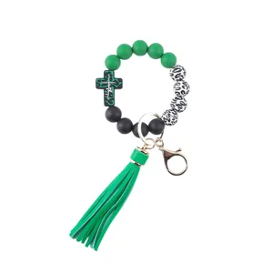 Detailed view of green silicone beaded wristlet keychain with cross charm and tassel.