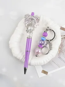 Macro view of elegant purple beaded pen and matching rhinestone keychain on white shell dish.