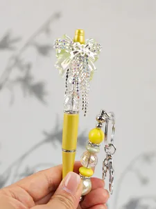 Detailed view of yellow beaded pen featuring a sparkling bow and rhinestone tassels set