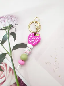 Close-up of pink apple silicone bead keychain with 'TEACH' engraving for Teacher's Day gift