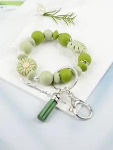 Nahaufnahme eines grünen Silikon-Schlüsselanhängers mit Gänseblümchen und Quaste