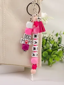 Detail van kralen sleutelhanger met DOG MOM en MAMA bedeltjes aan een crème lederen tas