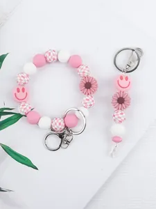 Silikon-Perlenarmband und Schlüsselanhänger-Set mit Blumen- und Smiley-Anhänger in Rosa.