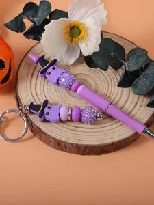 Close-up of cute purple ghost beaded pen and keychain set on a rustic wooden decorative stand