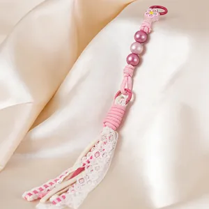 Detail showing handmade pink beaded charm with delicate lace tassel on satin background