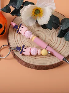 Detail of pink Halloween beaded pen and matching cute ghost keychain on a wood slice.
