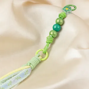 Detailed view of handmade green beaded keychain with floral fabric tassels and acrylic flower