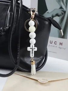 Detail of white silicone bead cross keychain with Jesus engraving on a black bag