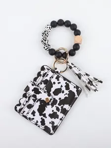 Detailed view of the cow print wallet keychain featuring beaded bracelet and tassel
