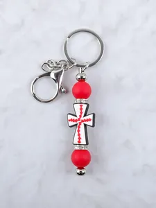 Detalle de llavero de cruz de silicona con cuentas rojas y espaciadores de strass.