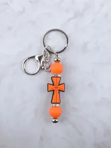 Detalle de un llavero de cruz de silicona naranja con pedrería y cierre de langosta.