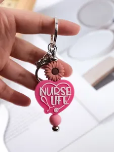Macro view of pink heart-shaped "NURSE LIFE" silicone keychain with daisy detail.