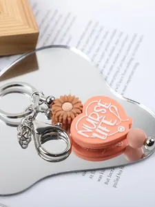 Close-up of a pink Nurse Life silicone heart keychain and brown daisy charm on mirror