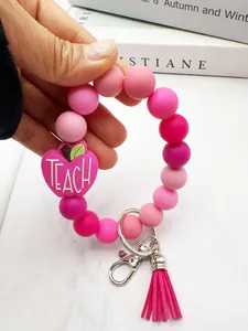 Detail view of pink silicone beaded keychain featuring apple charm and tassel held by hand.