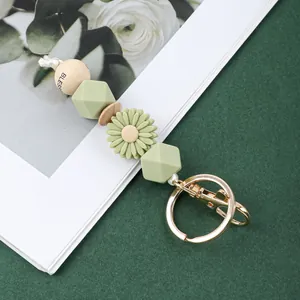 Détail de perles en silicone vertes et breloque marguerite sur porte-clés doré