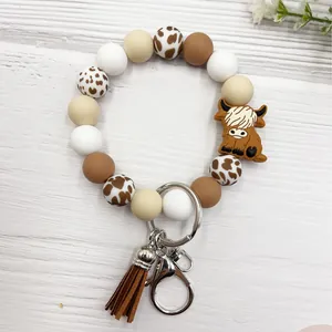 Highland cow silicone bead bracelet keychain with brown tassel on white wood background