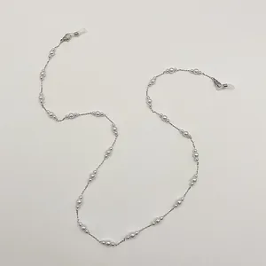 Détail élégant d'une chaîne en perles pour masque et lunettes avec des fermoirs argentés