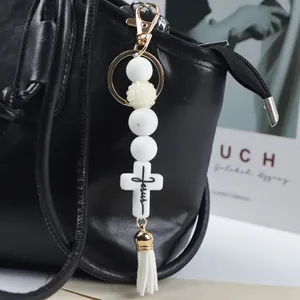 White silicone beaded cross keychain with tassel accessory on a black leather handbag
