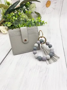 Close-up of a grey PU leather card holder with a silicone bead bracelet and tassel detail.