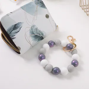 Bedrucktes Akkordeon-Kartenetui neben einem lila-grauen Silikonperlen-Armband-Schlüsselanhänger