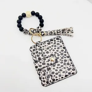 Detalle de porta tarjetas de leopardo con pulsera de cuentas de silicona y borla a juego.