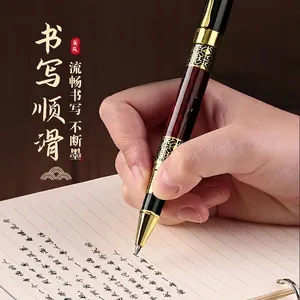 Elegant Chinese style metal business pen with gold patterns shown writing on paper.