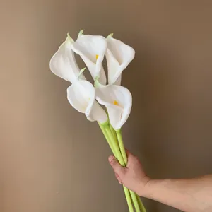 Hand holding a bouquet of five white PU calla lilies for wedding home decor.