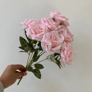 Detailed view of a nine-head pink artificial rose bouquet held by hand for scale.