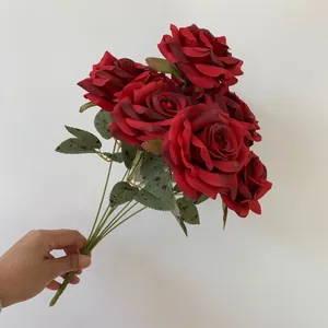 A hand holding a bunch of nine dark red artificial roses with realistic green leaves