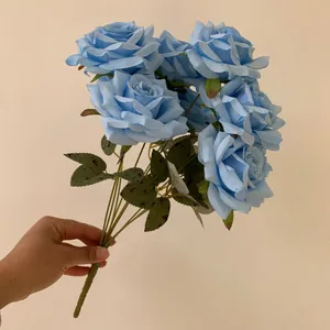 Detail view of a hand-held bouquet featuring nine light blue artificial roses and leaves