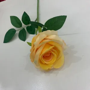 Nahaufnahme einer einzelnen gelben künstlichen Rose mit realistischen grünen Blättern