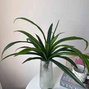 Close-up of realistic green artificial orchid leaves placed in a fluted glass vase on a table