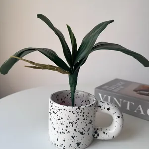 Macro view of realistic artificial orchid leaves placed in a stylish speckled ceramic mug